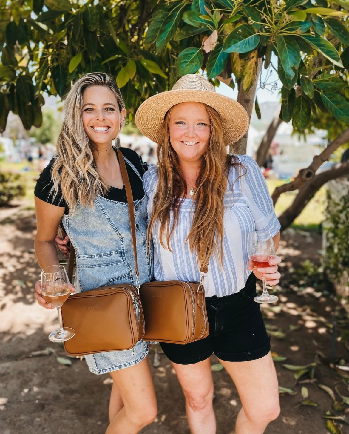 Two women holding wine glasses and wearing poppy crossbody diaper bags. 