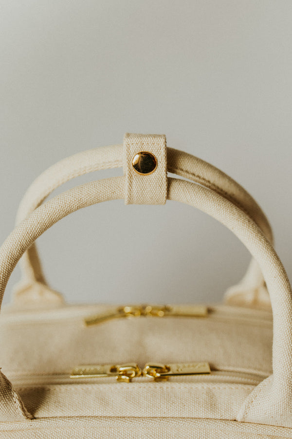 Close-up of natural color everyday poppy bag with gold accents on a neutral background